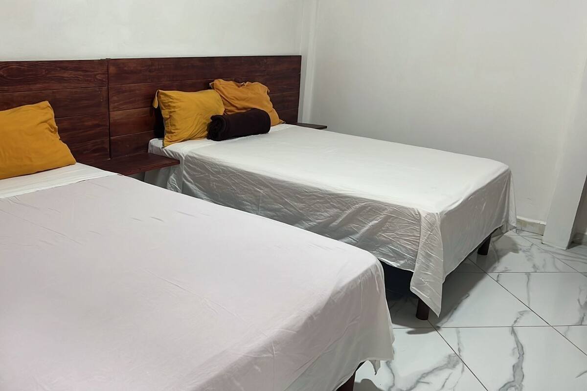Two single beds with white linens and wooden headboards, a nightstand, and a white wall.