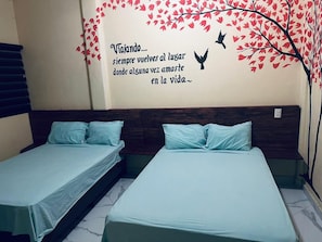 A room with two single beds, a wall with a tree and bird mural, and a wooden headboard. - Hotel NB aeropuerto (Puerto Vallarta)