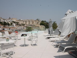 Una terrazza sul tetto con piscina, poltroncine da relax bianche e ombrelloni.