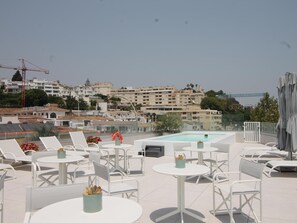 A rooftop terrace with lounge chairs and tables, a swimming pool, and a view of a cityscape with buildings and a bridge. - La Joya 1C. New apartment , 300 m from the beach (Torremolinos)
