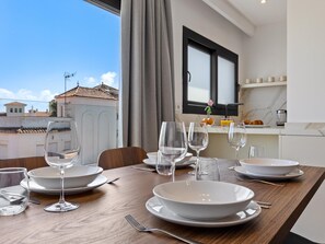 Un tavolo da pranzo apparecchiato con piatti, bicchieri e posate, con vista su edifici e una finestra con tende.