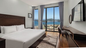 Een hotelkamer met een groot bed, een bureau, een stoel en uitzicht op zee.
