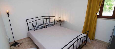 Une chambre à coucher avec un lit, une table de chevet, une lampe et une fenêtre avec des rideaux.