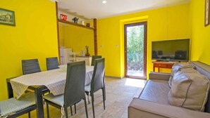 Un comedor con una mesa y sillas, un sofá, un televisor y una puerta que da al exterior.
