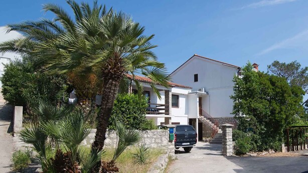 Una casa de dos pisos con un balcón, un muro de piedra y una camioneta estacionada.