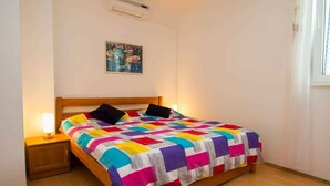 A single bed with a colorful quilt, a bedside lamp, a small wooden nightstand, and a wall-mounted air conditioner. - Holiday Apartment Zeljka A2 (Mali Lošinj)