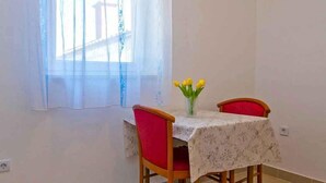 A dining area with a table, two chairs, and a window with curtains. - Holiday Apartment Zeljka A2 (Mali Lošinj)
