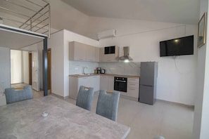 A modern kitchen with a dining area, built-in appliances, and a flat-screen TV. - Holiday Apartment Deluxe apartment studio 1/4 (Mali Lošinj)
