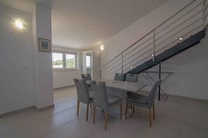 A modern dining area with a large table and chairs, a staircase, and a window providing natural light. - Holiday Apartment Deluxe apartment studio 1/4 (Mali Lošinj)