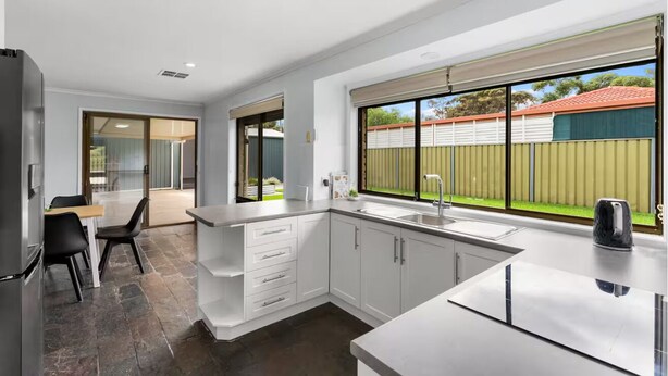 Eine moderne Küche mit weißen Schränken, einem großen Fenster und einem Essbereich mit Tisch und Stühlen.