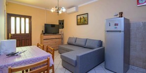 A compact living space with a sofa, a dining table with chairs, a television, a refrigerator, and a door with a window. - Holiday Apartment Sandra A2+1 (Veli Lošinj)