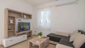 Ein Wohnzimmer mit Fernseher, Sofa und einem kleinen Tisch mit einer Pflanze.