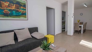 Ein Wohnzimmer mit einer Couch, einem gelben Hocker, einer Pflanze und einem Gemälde an der Wand.