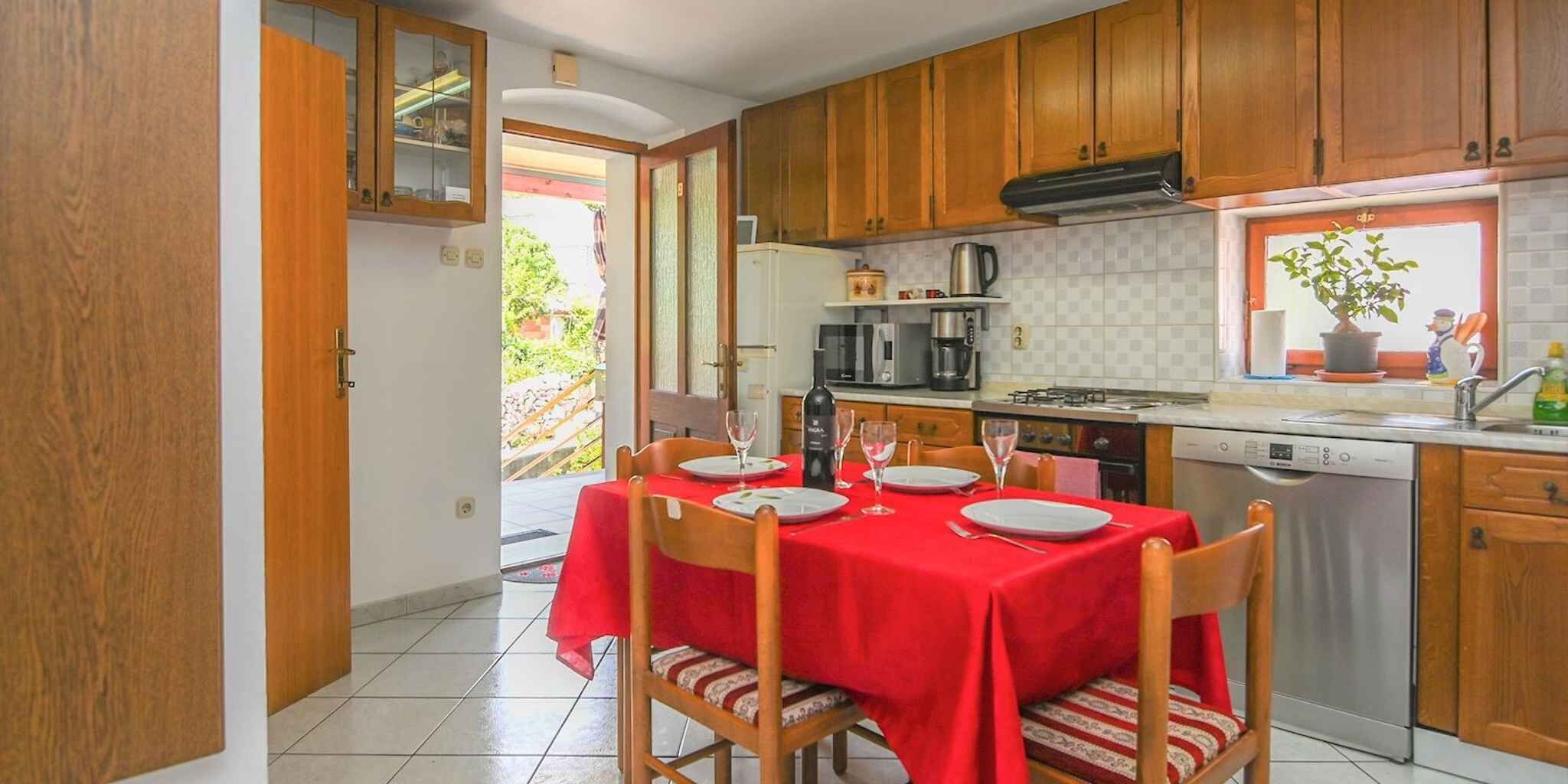 A kitchen with wooden cabinets, a dining table with red tablecloth, chairs, a stove, and a dishwasher.