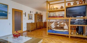 A room with a wooden floor, a glass table with a red object, a wooden cabinet with glass doors, and a model ship on display. - Holiday flat (Mali Lošinj)