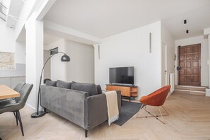 A modern living room with a sofa, TV, dining table, and a red chair. - Blueground | Le Marais, view, nr Place des Vosges (Paris)
