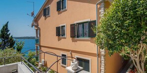 A multi-story building with balconies, a view of the sea, and a stone wall. - Holiday apartment (Mali Lošinj)