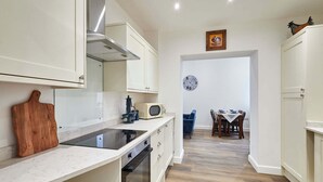 A kitchen with white cabinets, a microwave, and a wooden cutting board. - Host Stay The Stables Apartment 1 (Saltburn-by-the-Sea)