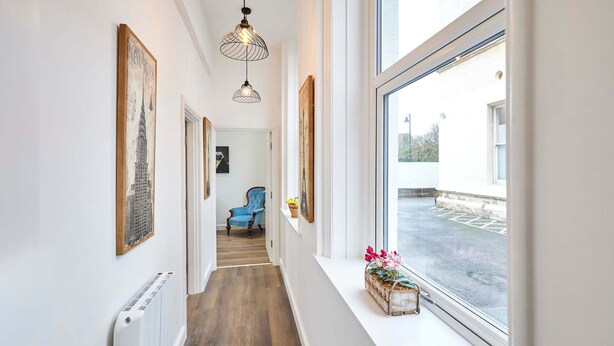 A hallway with a radiator, a blue chair, and a window with a view of a parking lot. - Host Stay The Stables Apartment 1 (Saltburn-by-the-Sea)