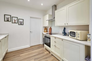 A kitchen with white cabinets, a microwave, and a wooden cutting board. - Host Stay The Stables Apartment 1 (Saltburn-by-the-Sea)