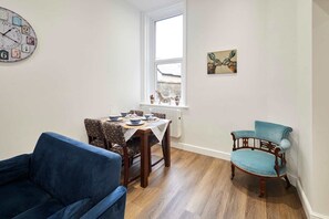 A dining area with a table set for four, a blue sofa, a wooden chair, and a wall clock. - Host Stay The Stables Apartment 1 (Saltburn-by-the-Sea)