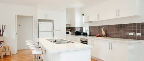 A modern kitchen with white cabinetry, a central island with bar stools, a built-in oven, and a microwave.
