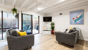 Una sala de estar moderna con dos sofás grises, un televisor de pantalla plana, un cuadro y un ventanal corredizo que da a un área exterior.