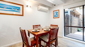 Un comedor con mesa y sillas de madera, paredes blancas y un ventanal con vista a una valla de madera.