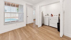 Una cucina pulita e moderna con elettrodomestici bianchi, pavimento in legno e vista su una piscina dalla finestra.