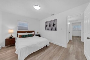 A bedroom with a bed, nightstand, lamp, wall art, and a door leading to another room. - Perfect 4-bedroom house with AC in enchanting Tampa (Tampa)