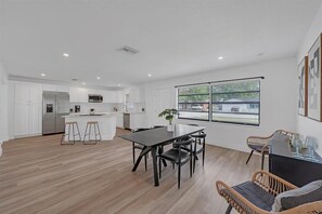 A modern kitchen with white cabinetry, a central island, and a dining area with a black table and chairs. - Perfect 4-bedroom house with AC in enchanting Tampa (Tampa)