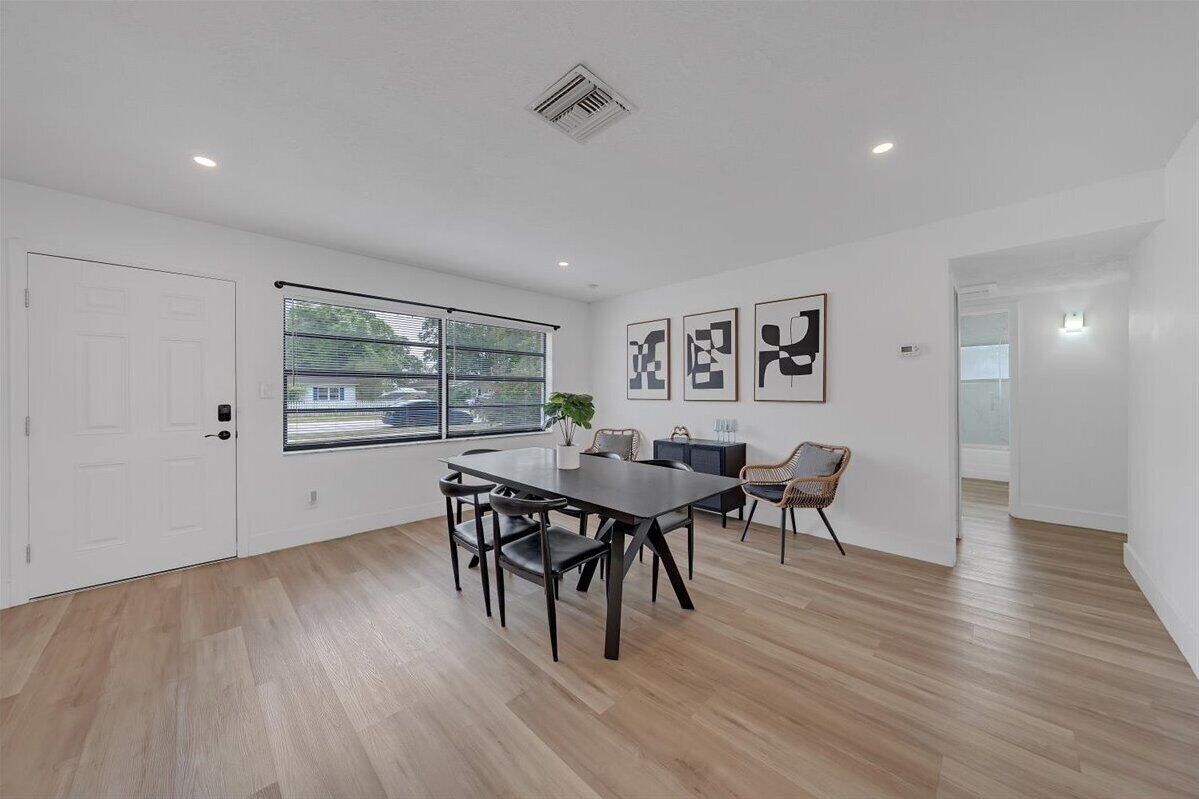 A spacious room with a large dining table, chairs, a potted plant, and artwork on the walls.