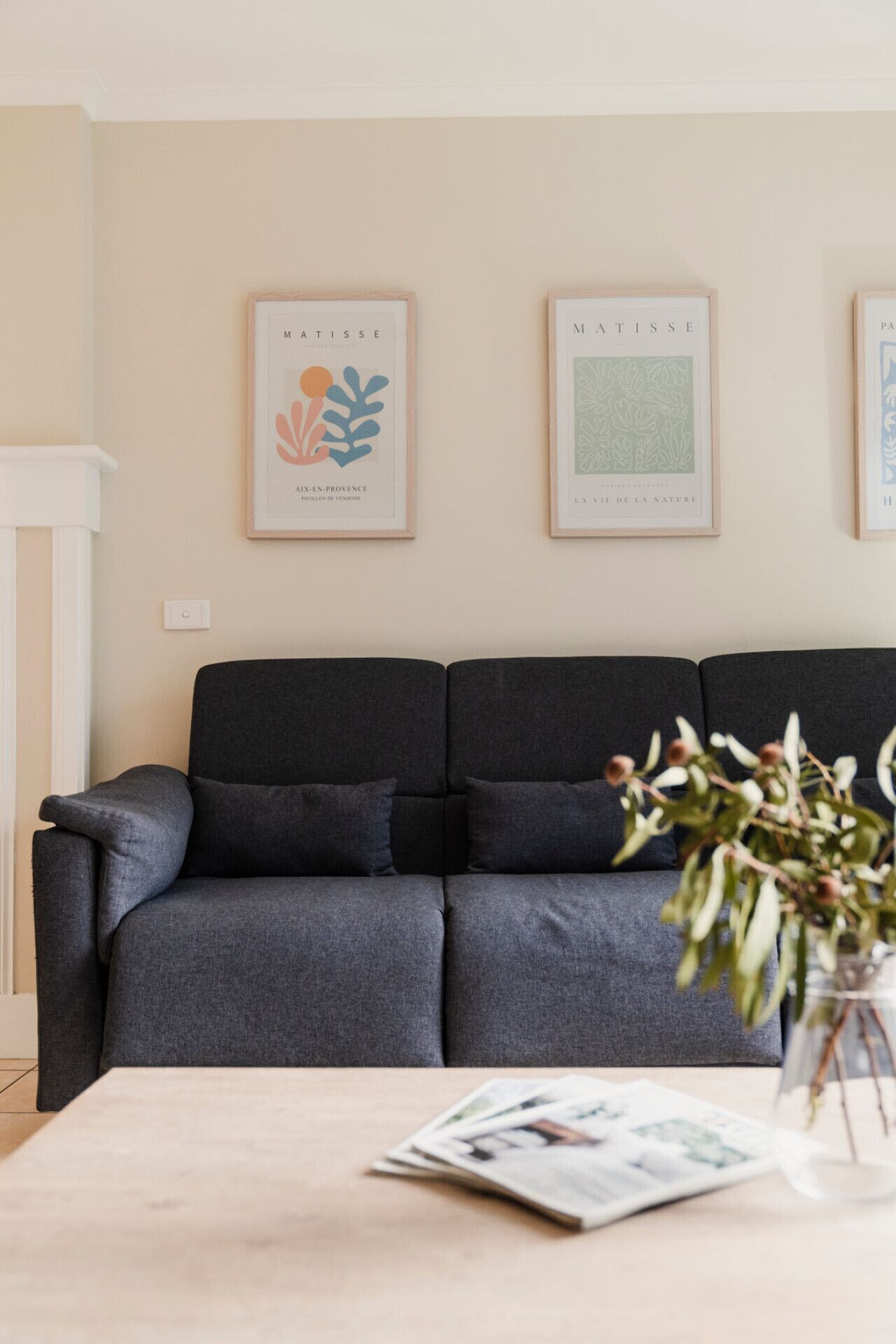 Ein modernes Wohnzimmer mit einem dunkelgrauen Sofa, einem weißen Beistelltisch und zwei gerahmten Kunstwerken an der Wand.
