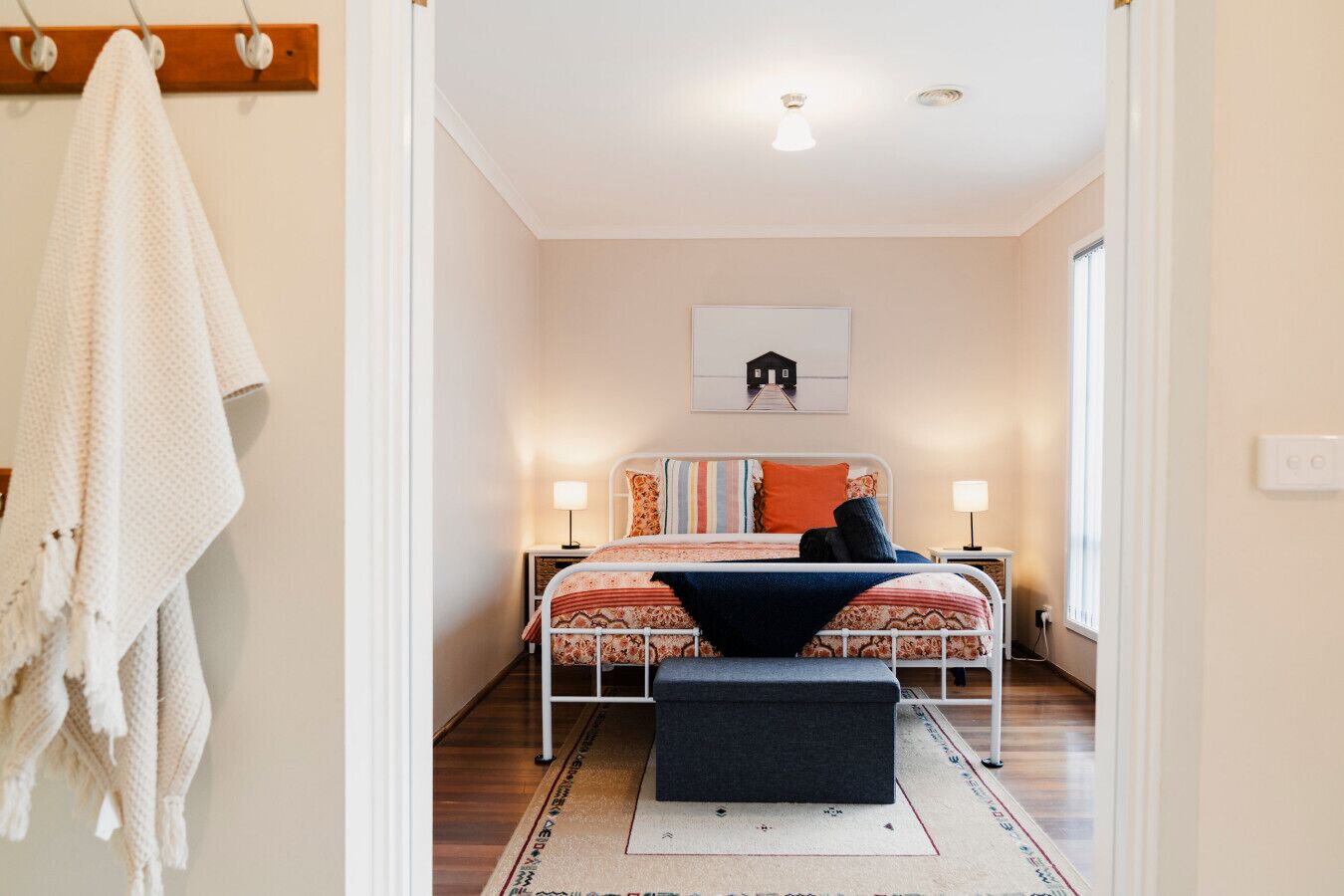 A bedroom with a bed, bedside tables, a wall-mounted artwork, and a hallway leading to another room.