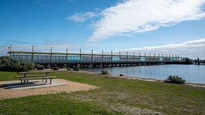 Un long pont piétonnier enjambant une étendue d’eau, avec un banc et une table de pique-nique au premier plan.