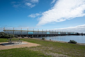 A long pedestrian bridge over water with a bench and picnic table in the foreground.