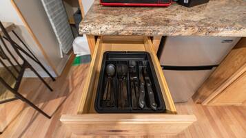 A kitchen with a drawer containing utensils, a microwave, and a refrigerator.