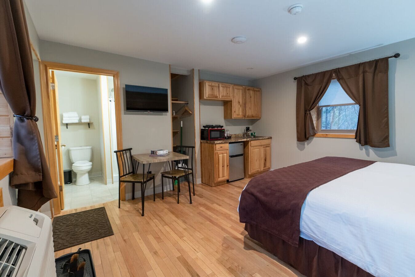 A compact room with a bed, a small dining table, chairs, a kitchenette, and a bathroom.