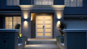Una casa moderna con puerta principal, dos luces exteriores encendidas y un pequeño jardín.