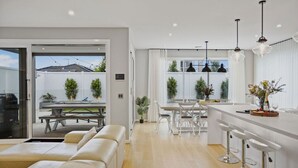 Una cocina moderna con encimeras blancas, taburetes de bar e iluminación colgante.