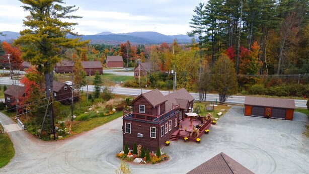 A two-story wooden house with a porch, surrounded by autumn foliage and a mountainous backdrop. - King Room Near Trails White Mountains Resort (Bethlehem)