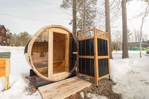 Een houten sauna met een open deur, een houten bank en een klein houten platform.