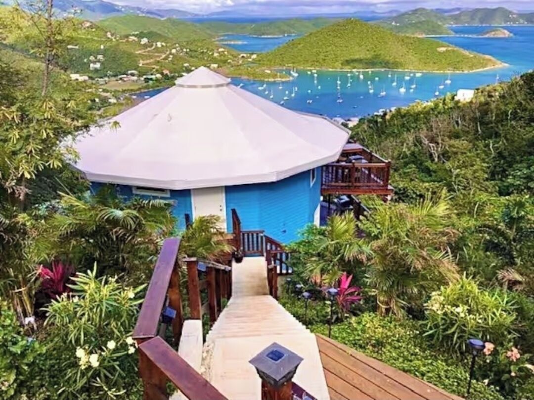 A resort with a central building, a wooden deck, and a view of the ocean and hills.
