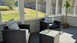 En overdækket terrasse med fletmøbler, en potteplante og udsigt til en baghave.