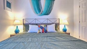 A bed with a geometric headboard, two bedside lamps, a hammock, and a patterned bedspread.
