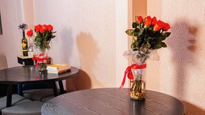 Un comedor con mesas redondas y sillas grises, cada una con un jarrón de flores rojas y una cinta roja.
