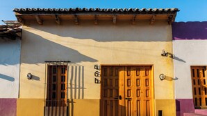 Un edificio con techo de tejas, puerta de madera y ventana con barrotes.