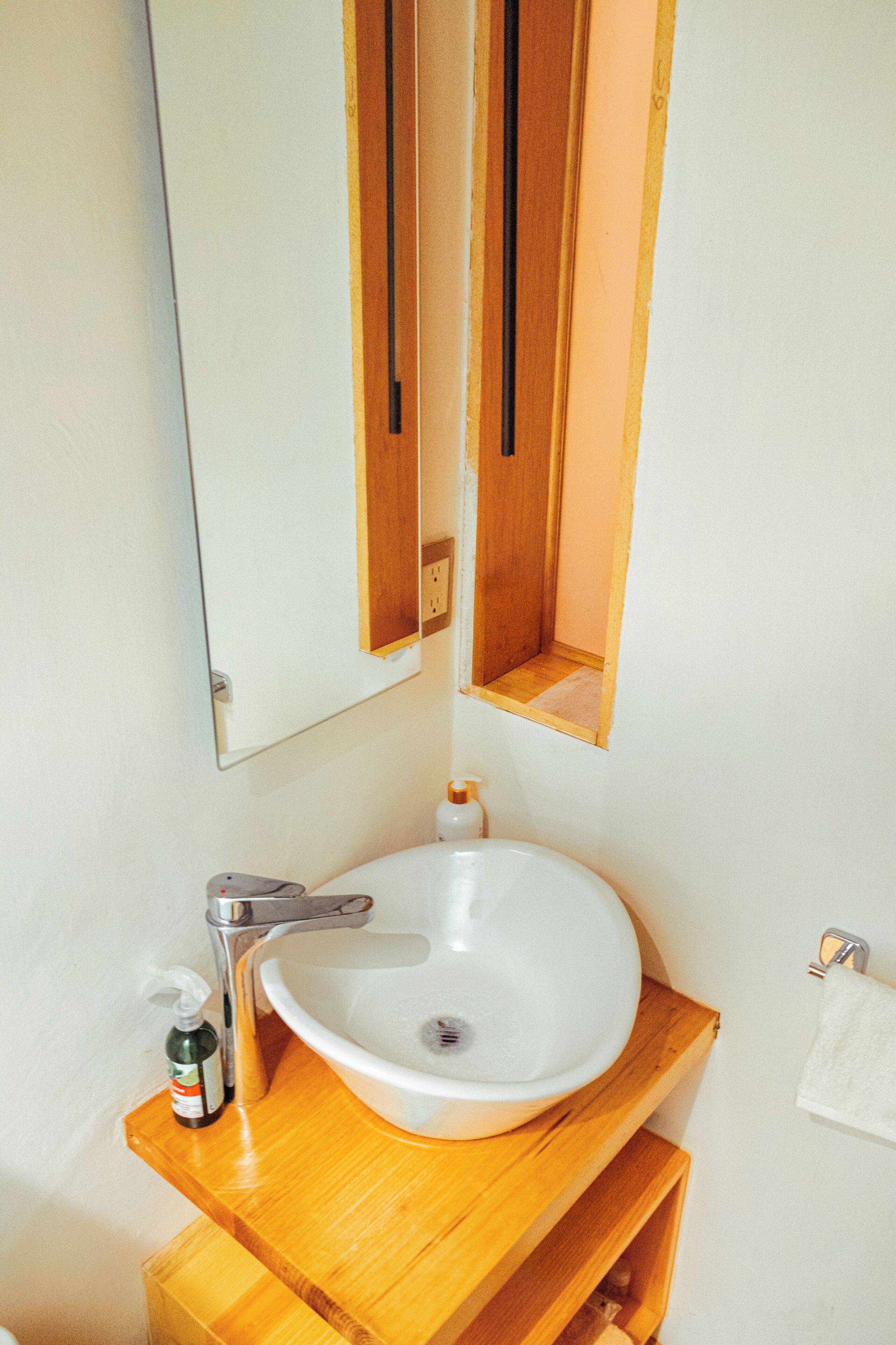 Un baño con lavamanos blanco, tocador de madera, un espejo y un perchero para toallas.