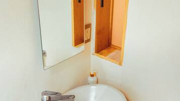 Un baño con lavamanos blanco, tocador de madera, un espejo y un perchero para toallas.