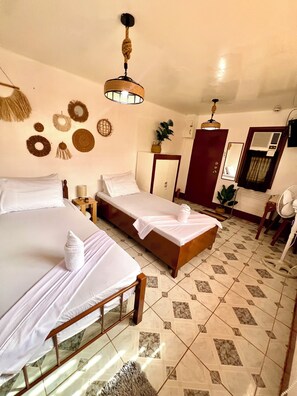 Ein Hotelzimmer mit zwei Betten, Holzboden, Deckenventilator, Spiegel und einer Tür mit Klimaanlage.